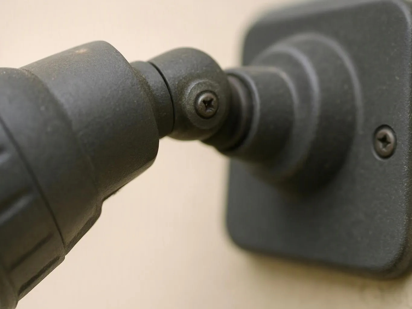 Close-up of a black adjustable wall-mounted fixture with a screw joint against a beige wall