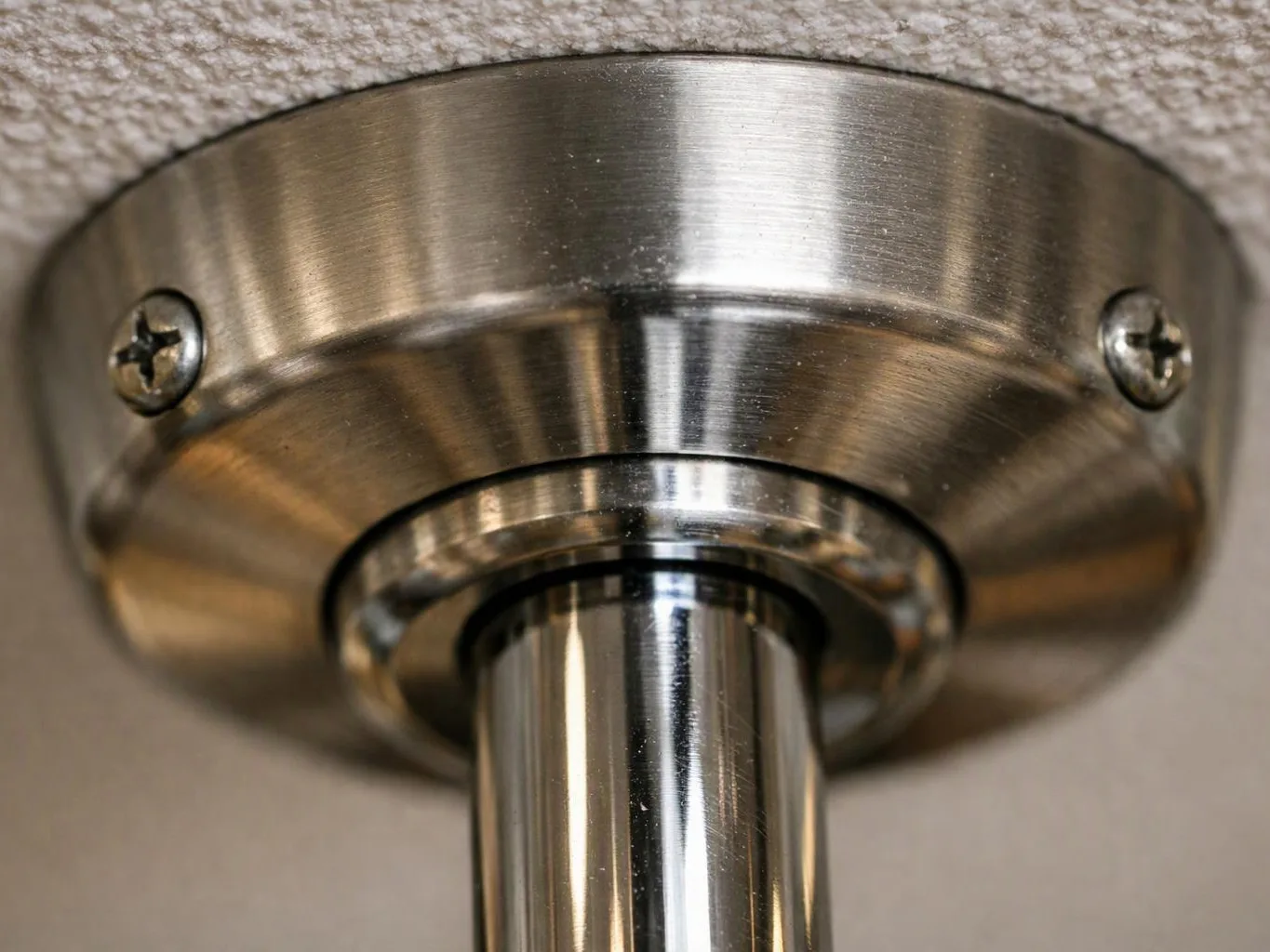 Close-up of a brushed metal ceiling fixture mount with two screws and a central tube
