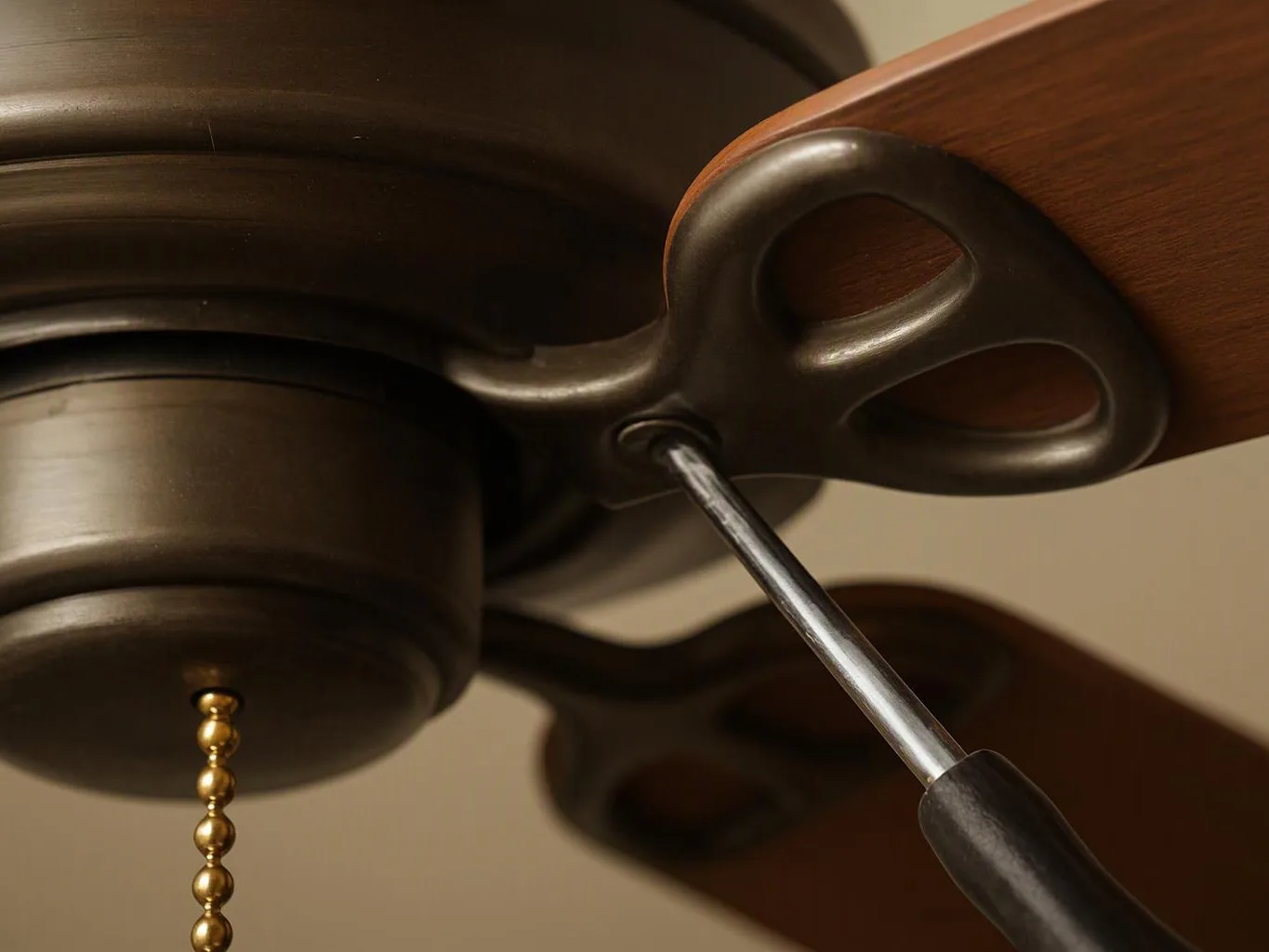 Close-up of a ceiling fan with a pull chain and screwdriver adjusting the wooden blade bracket