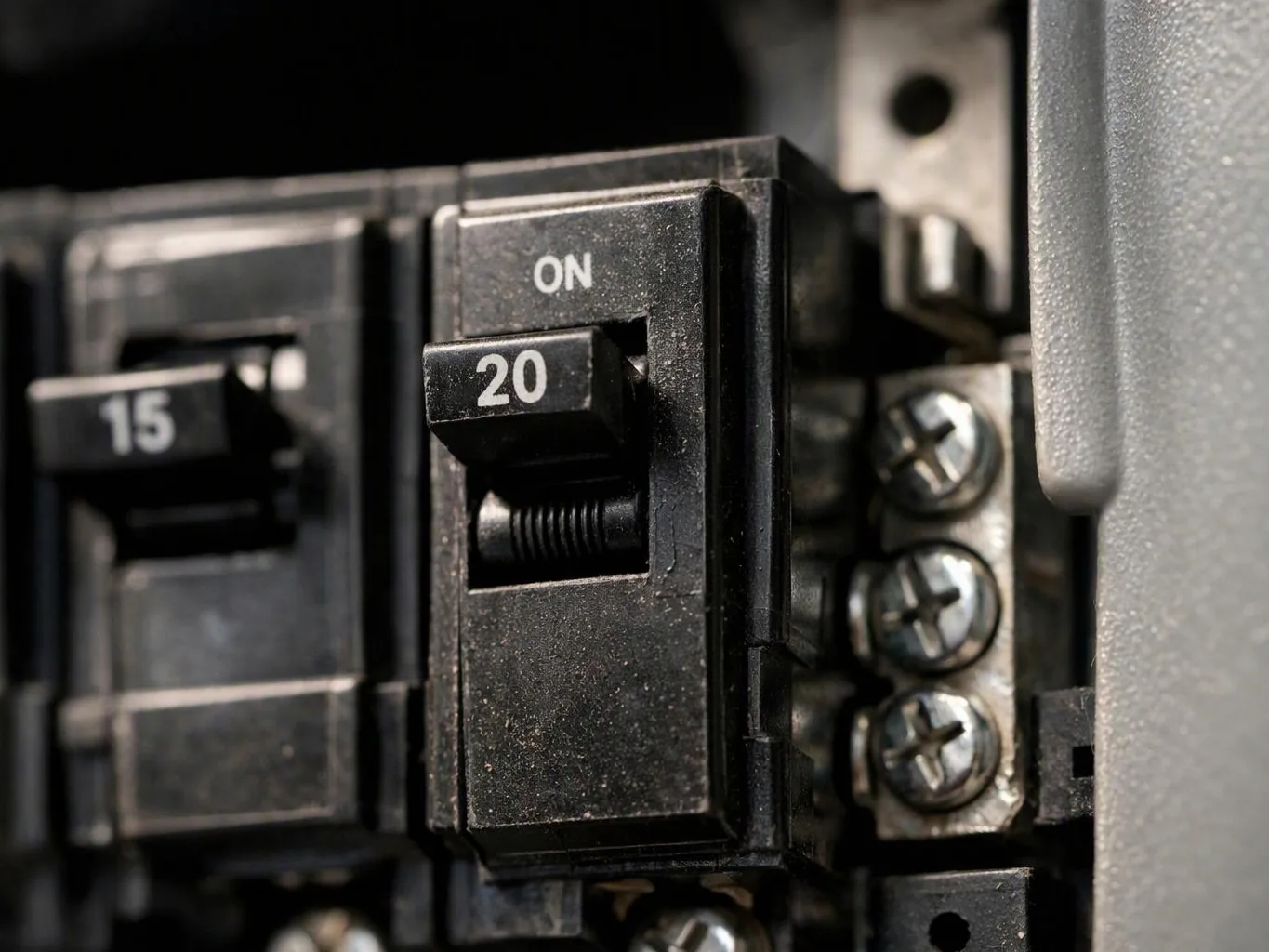 Close-up of a circuit breaker panel with numbered switches and metal screws inside a gray electrical box