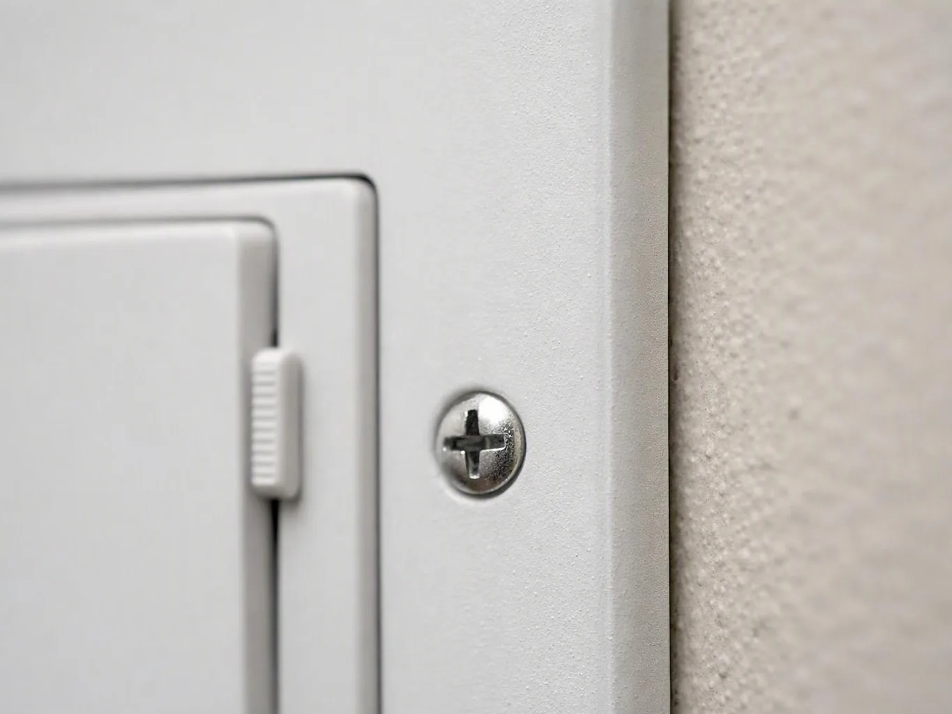 Close-up of a white light switch plate with a visible screw on a textured wall
