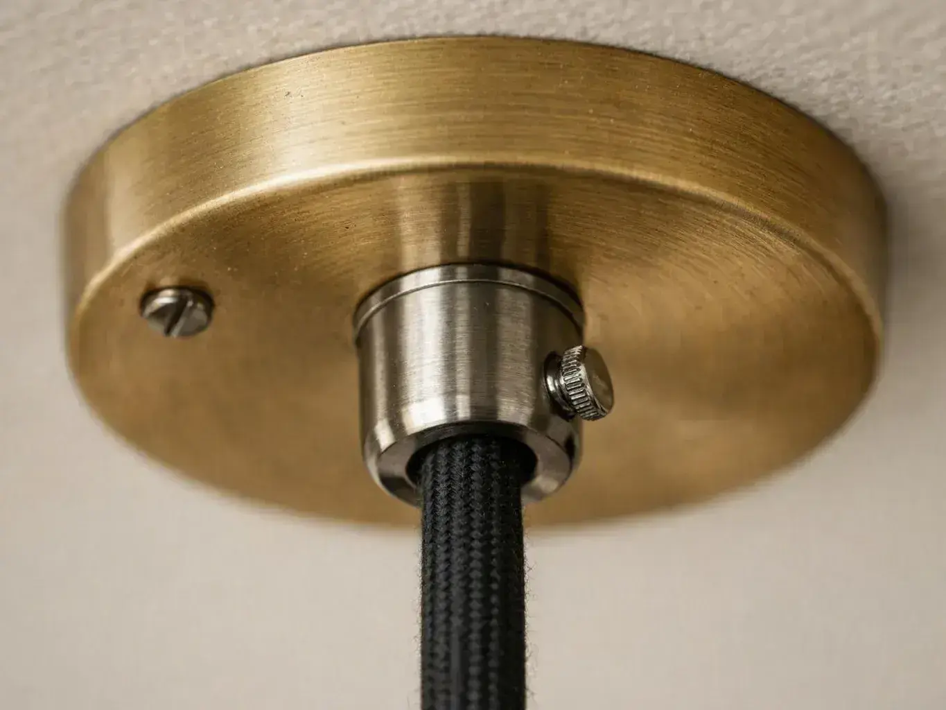 Brass ceiling canopy supports a black braided electrical cord against a white