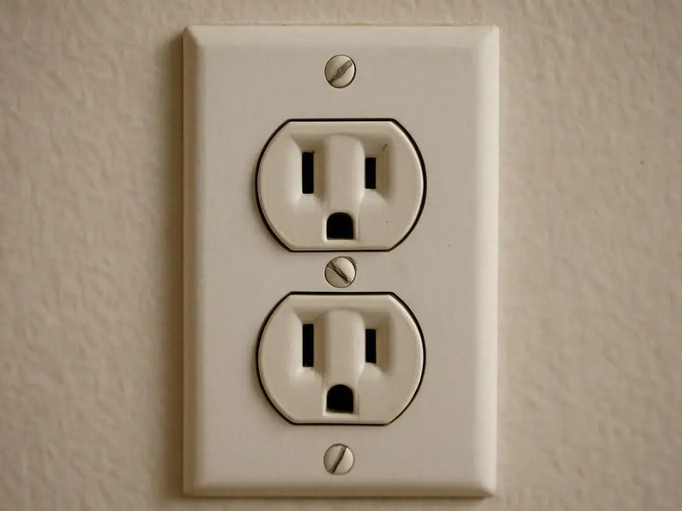 A white electrical wall outlet with two sockets is mounted on a beige textured wall