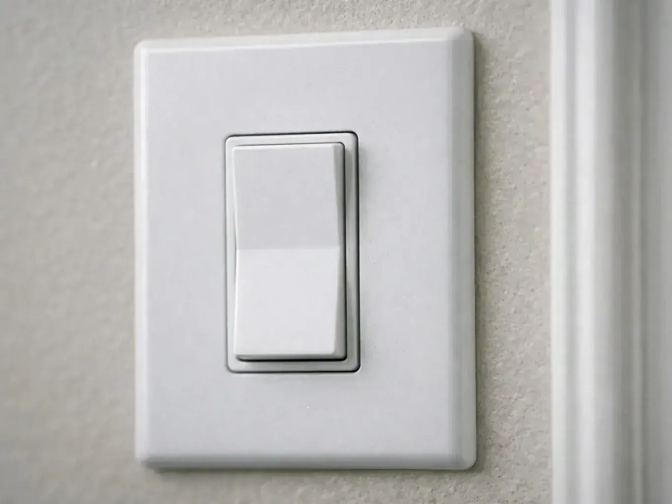 White light switch beside a door frame on a beige wall