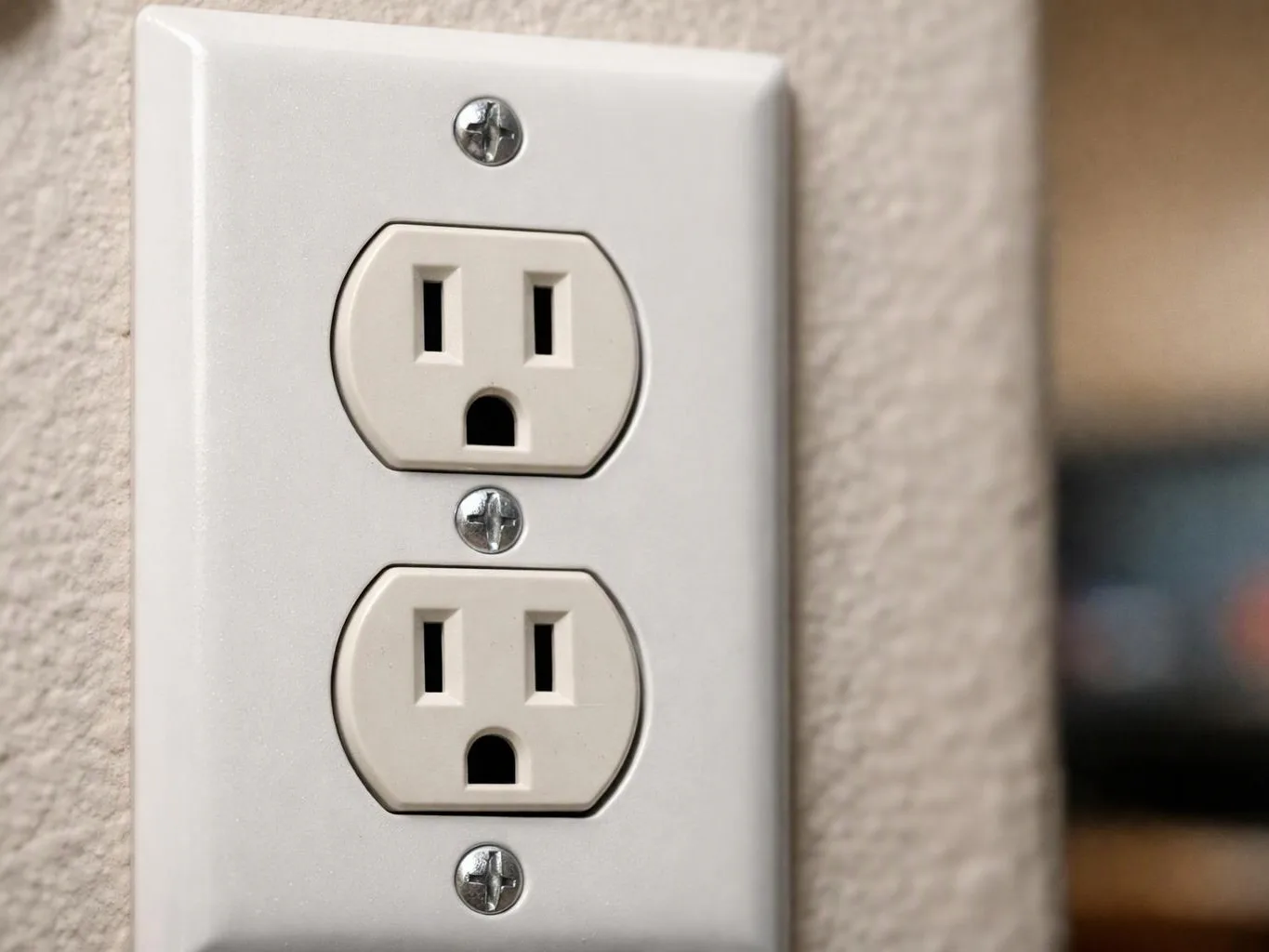 Two white electrical outlets sit on a wall plate against a textured beige wall, viewed close up