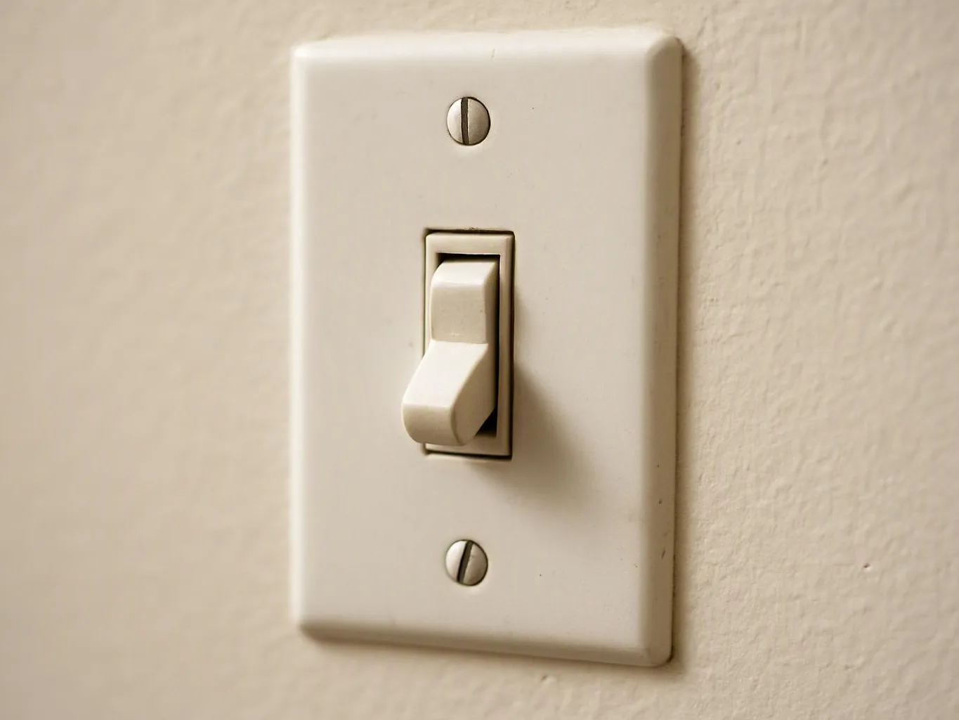 A white light switch sits on a beige wall, with the toggle in the down position